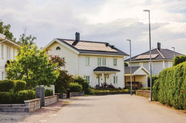 Çatı kiremit kaplı güneş panelleri olan, sessiz yerleşim yerlerinde yeşilliklerle çevrili beyaz, modern bir ev. İsveç.