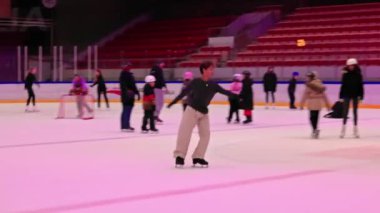 İnsanlar, merkezdeki adamın özel bir performans sergilediği kapalı alandaki buz pateninde kayıyorlar. Etrafındaki diğer patenciler de büyük arenada.. 