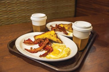 Miami Havaalanı 'ndaki bir kafede üzerinde domuz pastırması, sahanda yumurta, tost ve kahve fincanları olan tabaklar..