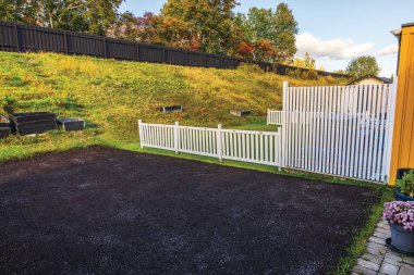 Restored lawn area in backyard garden with white fence and wooden flower beds, preparing for autumn growth. Sweden.