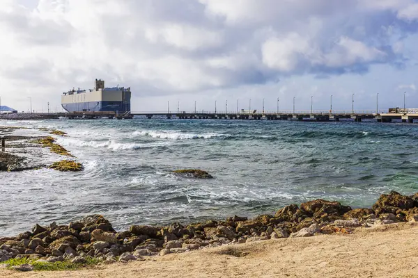 stock image Cargo ship docked at a pier with waves hitting rocky shore and cloudy skies, located on the coast of Curacao island in the Caribbean Sea. 