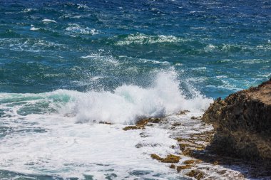 Dalgalar Aruba 'da kayalık bir kıyı şeridine çarpıyor. Karayip Denizi' nin açık mavi suları güneşli gökyüzünün altında..