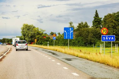 Otoyolda giden arabalar açık gökyüzünün altında hız kamerası uyarı işaretleri ve yol işaretleriyle. 