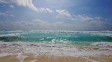 Dalgalar Karayip Denizi 'ndeki parçalı bulutlu gökyüzünün altında yavaşça kumlu kumsala yuvarlanıyor..