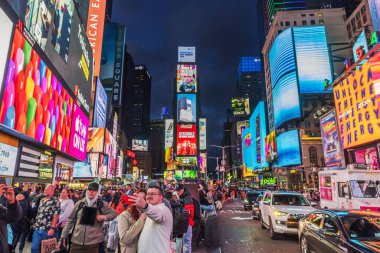 Gece Times Meydanı 'nda selfie çeken turistler, parlak reklam panoları, trafik ve canlı şehir ışıklarıyla çevrili. - New York. ABD.