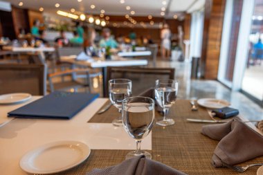 Suyu ve tabağı olan şık bir restoran masası. Yumuşak ışıklandırmalı ve arka planda bulanık yemek yiyen insanlar. Meksika.