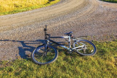 Dağ bisikleti çimenli yol kenarında güneşli bir günde kırsal kesimde çakıl yolunun yanında duruyor. İsveç. 