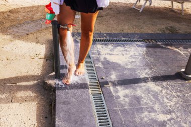 Woman rinsing sandy feet under beachside shower after day on sand. Curacao.  clipart