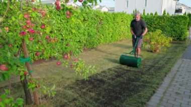 Bahçede süzgeç kullanarak taze toprak yayarak çimleri restore eden adam.. 