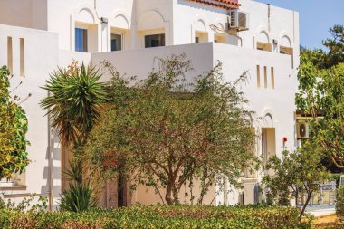 Akdeniz tarzı bina güneşli bir günde yeşil çalılar, bitkiler ve ağaçlarla çevrili. Girit. Yunanistan.