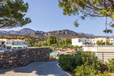 Havuz ve şezlonglarla çevrili, berrak gökyüzünün altındaki kayalık dağlar manzaralı bir tatil yeri. Girit. Yunanistan. 