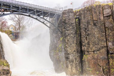 Paterson Büyük Şelalesi baharda bulutlu gökyüzünün altındaki kayalıklardan yükselen sisle birlikte. New Jersey 'de. ABD.