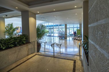 Geniş bir otel lobisi. Büyük cam girişi, yeşilliği ve modern dekoru var. Hoş geldin atmosferi sunuyor. Miami Plajı. ABD. 