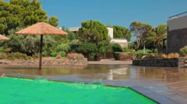 Rüzgarlı bir günde Girit Adası 'nda sazdan şemsiyeli ve yemyeşil otellerin bulunduğu açık havuz bölgesi..