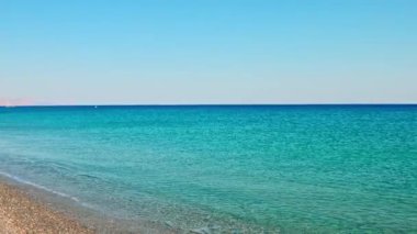 Girit adasındaki Akdeniz kıyısındaki çakıl taşı plajı, berrak turkuaz su ve uzak dağlarla.