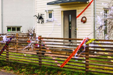 Front yard with Halloween decor, caution tape, cobwebs, and large spider on wall by door. Sweden. clipart