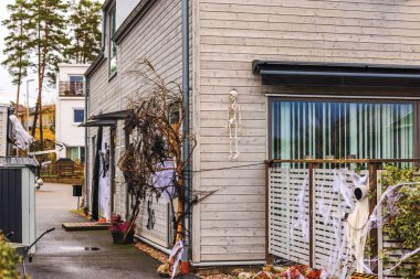 Halloween decorations on house wall with skeleton, ghostly figures, cobwebs, and spooky branches along pathway. Sweden. clipart