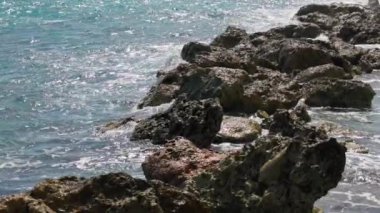 Dalgalar, arka planda açık mavi suyla kayalık Karayip kıyı şeridine çarpıyor. Ağır çekim. Curacao
