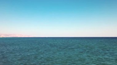 Yunanistan 'ın Girit adasında berrak mavi su, uzak dağlar ve çakıl taşı plajlı Akdeniz manzarası.