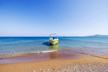 Açık mavi Ege Denizi 'nde kayalık plajlı, parlak yaz gökyüzünün altında demirli sarı bir tekne. Rodos, Yunanistan. 