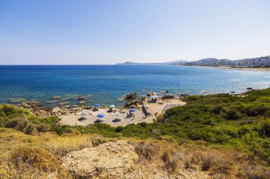Yunanistan 'ın Rodos adasında şemsiyeler, güneşlikler, kayalık kayalıklar ve Ege Denizi manzaralı tenha bir plaj. Rodos. Yunanistan. 