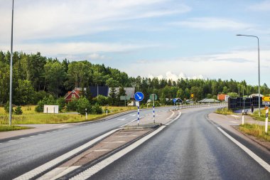 Trafik işaretleri ve uzak villaları olan boş otoyol, parçalı bulutlu gökyüzünün altında yeşil ağaçlarla çevrili.. 