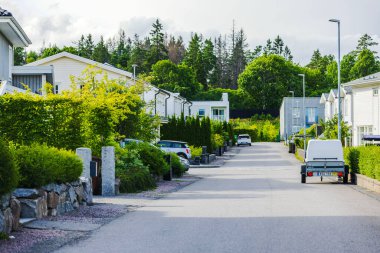 Yeşil çitlerle kaplı sessiz bir banliyö caddesi yol boyunca park etmiş arabalar ve ağaçlarla çevrili modern villalar..