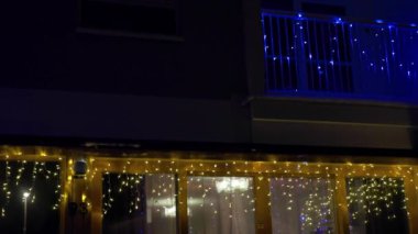 Gece gösterişli tel ışıklarla dekore edilmiş evin yakın görüntüsü, balkon ve pencereler aydınlatılıyor. İsveç.