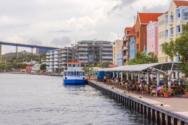 Tim Anna körfezi rıhtımı feribot ve renkli kafeleri ile Willemstad limanı, Curacao, bulutlu gökyüzünün altında. 
