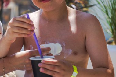 Anne açık havada güneşli bir yaz günü elinde samanla içki tutarken çocuklara güneş kremi sürüyor..