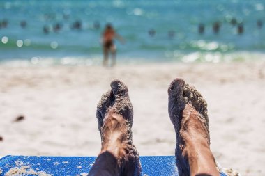 Miami Plajı 'nda güneşli bir yerde dinlenen kumlu erkek ayakları Atlantik Okyanusu' nda ve arka planda bulanık.. 
