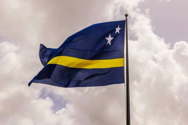 Rüzgarlı bir günde bulutlu gökyüzüne karşı bayrak sallayan Curacao bayrağı.