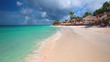 Turkuaz suyu olan tropik plaj Karayipler 'in kumlu kıyı şeridi ve bulutlu mavi gökyüzünün altında palmiye yaprağı şemsiyeleri. Aruba.