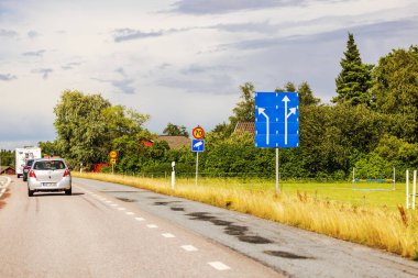 Hareket halindeki arabaları, yol işaretleri ve bulutlu gökyüzünün altında yeşil bitki örtüsü olan kırsal alanda otoyol.