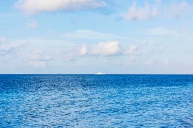 Açık mavi gökyüzünün altında beyaz bulutlarla çevrili askeri gemiyle Karayipler 'in deniz manzarası. Aruba.