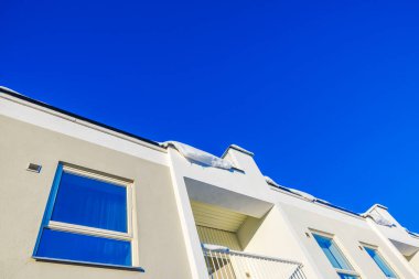 Güneşli kış gününde, karla kaplı çatısı ve açık mavi gökyüzü olan modern yerleşim yeri cephesi. İsveç.