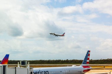 American Airlines airplane taking off from runway under overcast sky, captured near terminal with parked aircraft. Cancun. Mexico.  clipart