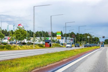 Ticari alandan geçen araçlarla dolu yoğun bir yol. Dükkanlar, bulutlu arka planda işaretler var..