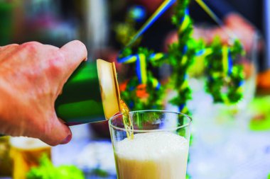 Man pouring beer from green can into glass during traditional Swedish Midsummer celebration with blurred festive decorations. clipart