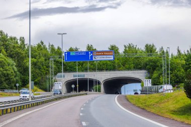 Bulutlu gökyüzünün altında yeşil ağaçlarla çevrili bir tünele çıkan otoyol girişi.. 