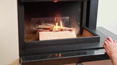 Ateş yakmak için modern şöminenin içindeki alevlere odun ekliyorlar. İsveç.  