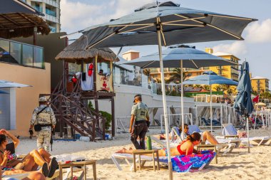 Soldiers and police patrol beach near lifeguard tower, ensuring safety for resort guests relaxing under umbrellas by Caribbean Sea. Cancun. Mexico.  clipart