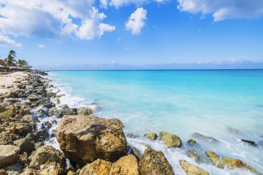 Turkuaz Karayip Denizi ve açık mavi gökyüzü ile Aruba 'daki tropikal plajın kayalık kıyı şeridi.