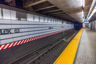 New York 'taki Lex 63 metro istasyonunda temiz fayanslı duvarlar, parlak sarı güvenlik şeridi ve boş raylar var. - New York. ABD. 