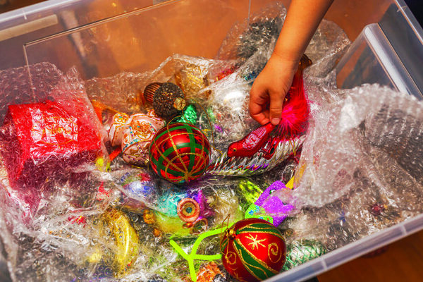 Child's hand reaching for red bird Christmas ornament in storage box filled with colorful festive decorations. Sweden.