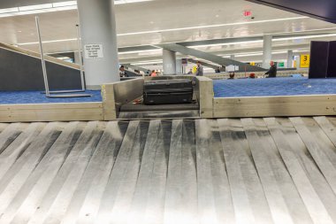 Modern havaalanı terminalindeki bagaj atlıkarıncasında arka planda bekleyen yolcularla birlikte siyah bavul ortaya çıkıyor. ABD. New York. 