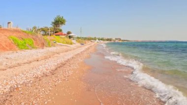 Yeşil tepeler ve açık gökyüzünün altındaki kızıl kayalıklarla çevrili Ege Denizi boyunca yumuşak dalgaları olan kumsal. Yunanistan.