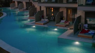 Night view of private pool terraces at Portes Lithos Luxury Resort with ambient lights reflecting on water. Halkidiki, Greece. 