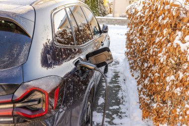 Kışın açık arazideki özel villanın otoparkında elektrikli araba şarj oluyor. İsveç.