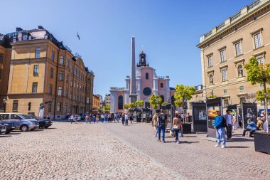 İsveç Ulusal Günü kutlamaları sırasında tarihi binalar, İsveç bayrağı ve açık hava sergisiyle kalabalık şehir meydanı. 